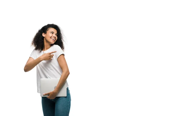 Щаслива молода афроамериканка вказує пальцем, тримаючи ноутбук ізольовано на білому — стокове фото