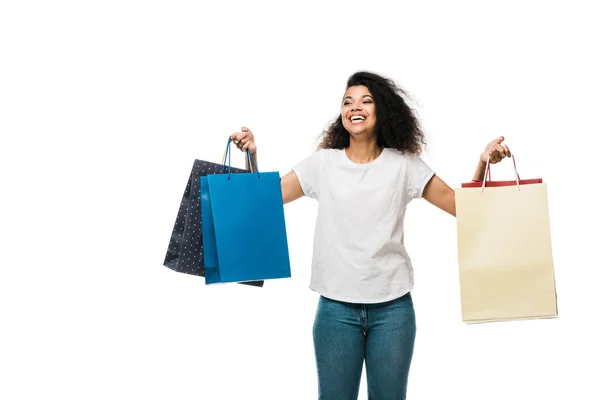 Chica afroamericana positiva sosteniendo bolsas de compras mientras está de pie aislado en blanco - foto de stock