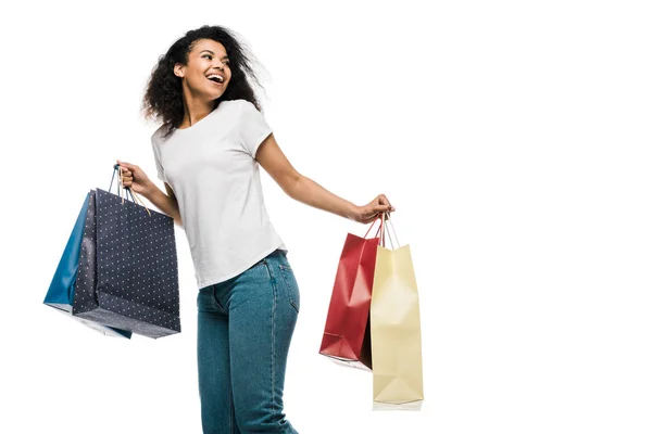Весела кучерява афроамериканська дівчина тримає сумки для покупок ізольовано на білому — стокове фото
