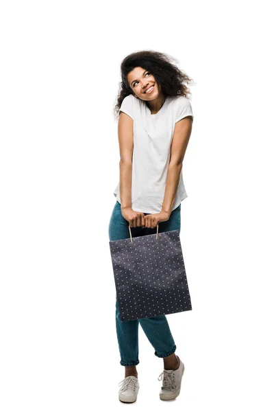 Cheerful african american girl holding shopping bag while standing isolated on white — Stock Photo