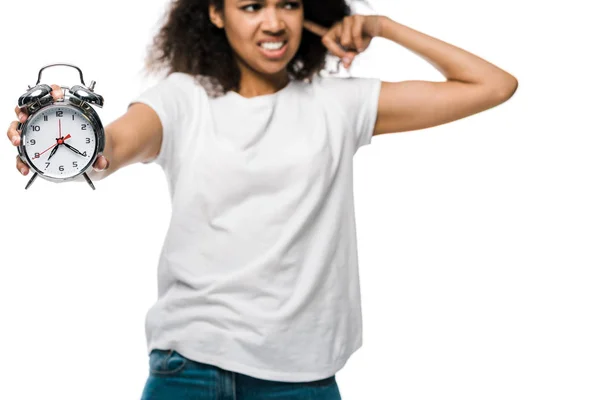 Foco seletivo do despertador vintage na mão da menina afro-americana encaracolada descontente cobrindo orelha isolada no branco — Fotografia de Stock