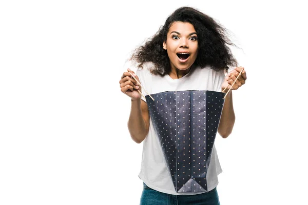 Shocked african american girl holding black shopping bag isolated on white — Stock Photo