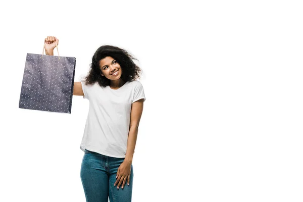 Glücklich lockige afrikanisch-amerikanische Mädchen hält schwarze Einkaufstasche isoliert auf weiß — Stockfoto