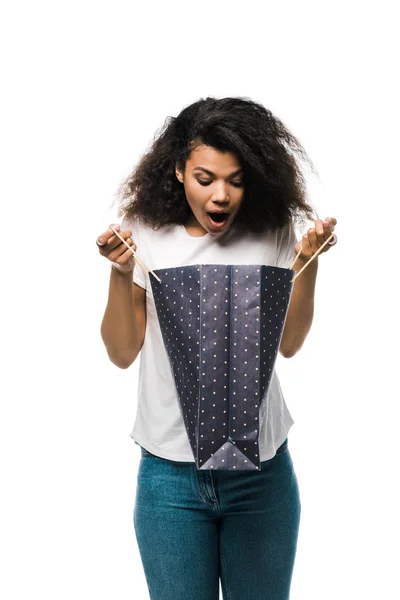 Shocked curly african american girl holding black shopping bag isolated on white — Stock Photo