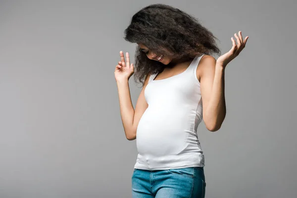 Fröhliche schwangere afrikanisch-amerikanische Mädchen Blick auf Bauch auf grau — Stockfoto