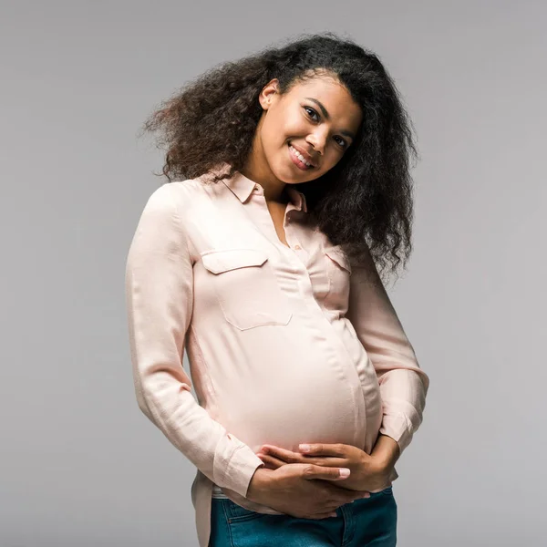 Mujer afro americana embarazada positiva tocando vientre aislado en gris - foto de stock