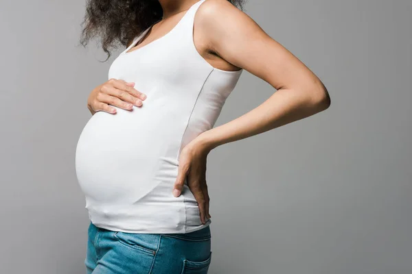 Vista ritagliata della giovane donna africana americana incinta che tocca la pancia sul grigio — Foto stock