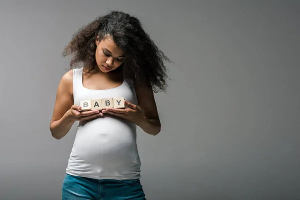 Pregnant african american woman standing and holding wooden cubes with baby lettering  on grey — Stock Photo