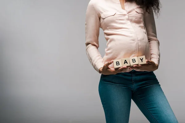 Vue recadrée de fille afro-américaine tenant des cubes en bois avec des lettres de bébé sur gris — Photo de stock