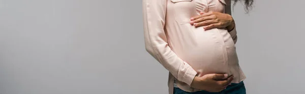 Panoramic shot of pregnant african american woman touching belly while standing on grey — Stock Photo