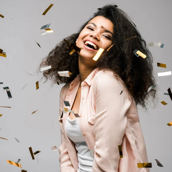 Happy african american girl smiling near shiny confetti on grey — Stock Photo