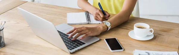 Panoramic shot of african american woman holding pen near notebook and laptop — Stock Photo