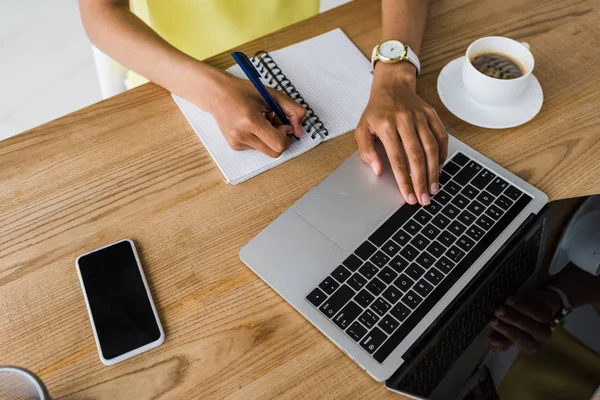 Overhead view of african american woman holding pen near notebook and laptop with blank screen — Stock Photo