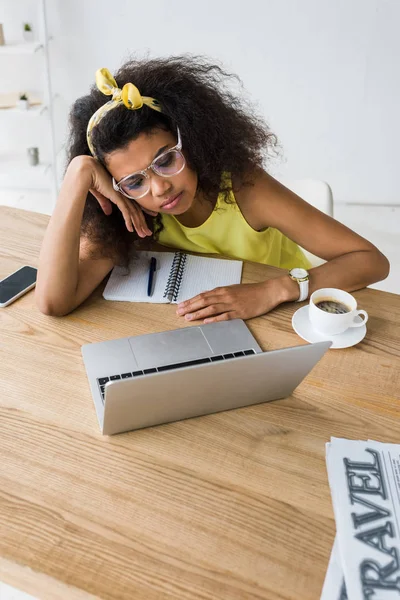 Вид сверху на молодую африканскую американку в очках, смотрящую на ноутбук возле чашки кофе — стоковое фото