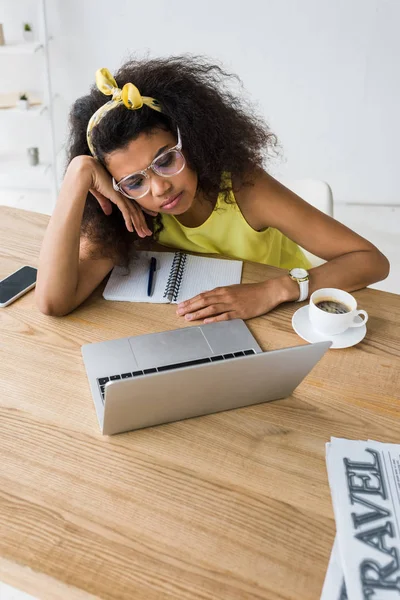 Overhead-Ansicht einer jungen afrikanisch-amerikanischen Frau mit Brille, die in der Nähe einer Tasse Kaffee auf ihren Laptop blickt — Stockfoto