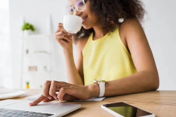 Selective focus of young african american woman drinking coffee near laptop — Stock Photo