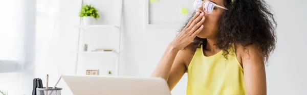 Colpo panoramico di stanca donna afroamericana in occhiali sbadigliando e coprendo la bocca — Foto stock