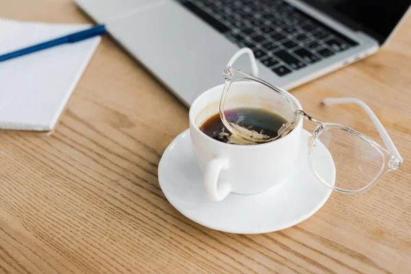 Foco seletivo de pires e xícara de café perto do laptop — Fotografia de Stock