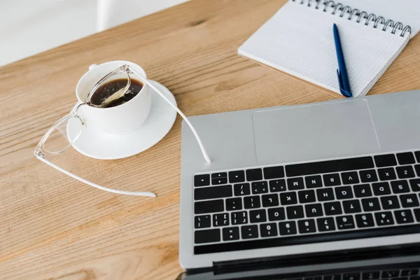 Selective focus of saucer and cup of coffee near laptop and notebook — Stock Photo