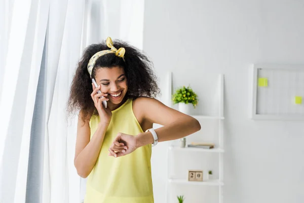 Alegre encaracolado Africano americano mulher falando no smartphone e olhando para assistir — Fotografia de Stock