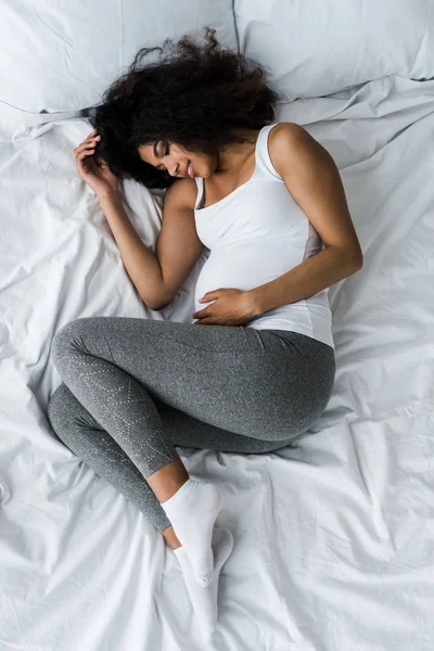 Vue de dessus de la femme enceinte afro-américaine avec les yeux fermés couché sur le lit — Photo de stock
