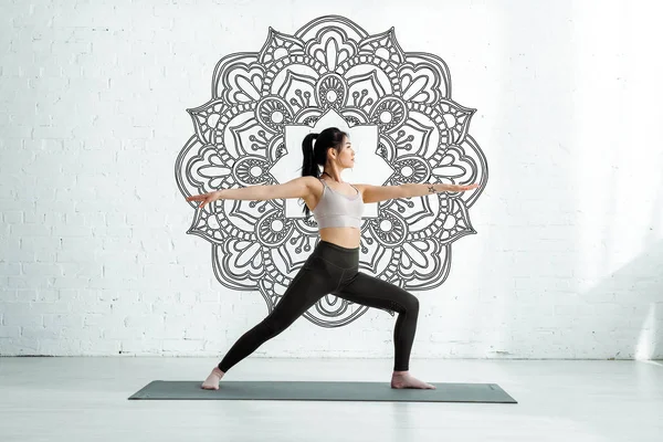 Calma mujer asiática de pie con las manos extendidas en yoga estera cerca mandala ornamento - foto de stock