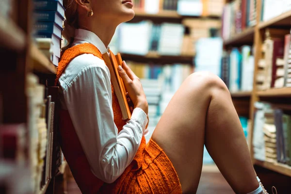 Vue recadrée de la femme en robe orange tenant livre dans la bibliothèque — Photo de stock