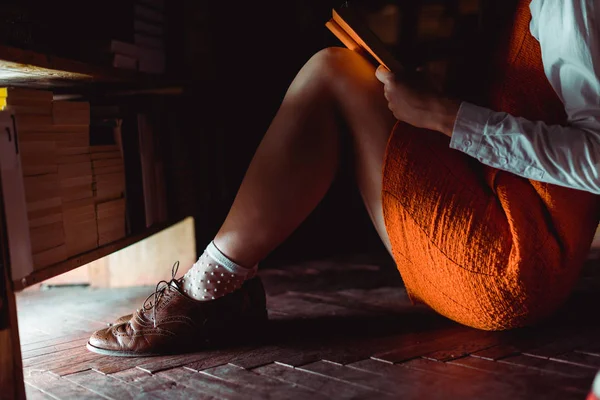 Обрізаний вид жінки, що сидить на дерев'яній підлозі і тримає книгу в бібліотеці — стокове фото