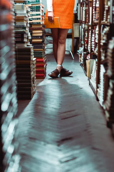 Обрізаний вид жінки, що тримає помаранчеву книгу в бібліотеці — стокове фото