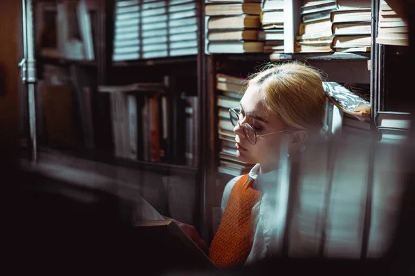Селективный фокус красивой блондинки, читающей книгу в библиотеке — стоковое фото