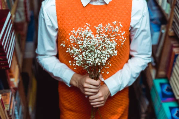 Cropped view of woman in orange dress holding white flowers in library — Stock Photo