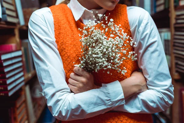 Teilansicht einer Frau mit verschränkten Armen, die weiße Blumen in der Bibliothek hält — Stockfoto