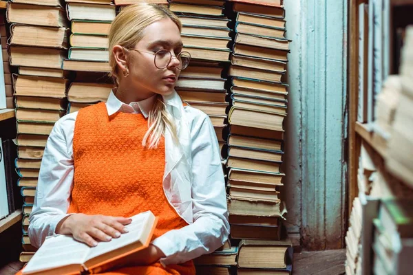 Mulher loira e atraente com olhos fechados em óculos segurando livro na biblioteca — Fotografia de Stock