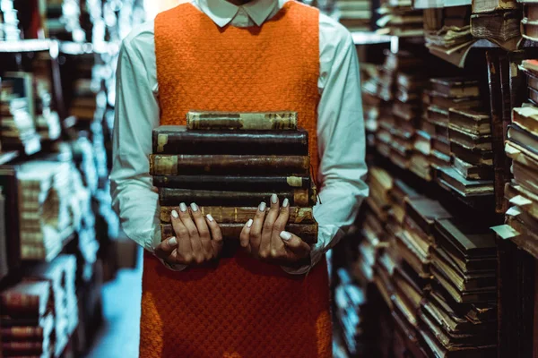 Vista cortada de mulher em vestido laranja segurando livros retro na biblioteca — Fotografia de Stock