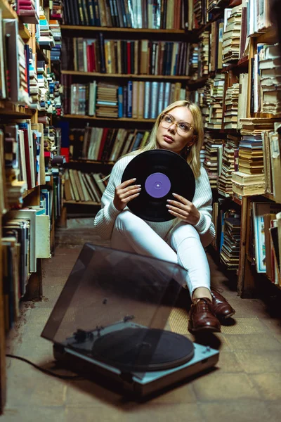 Pretty and blonde woman looking away and holding vinyl in library — Stock Photo