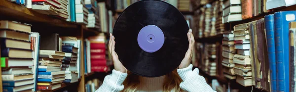 Panoramic shot of young adult woman holding vinyl in library — Stock Photo