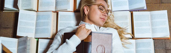 Panoramic shot of beautiful woman in glasses with closed eyes lying and holding book — Stock Photo