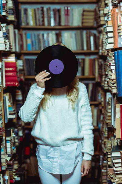 Mujer joven adulta en suéter blanco sosteniendo vinilo en la biblioteca - foto de stock