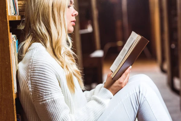 Vue latérale du livre de lecture de pull blanc blonde et jolie femme dans la bibliothèque — Photo de stock