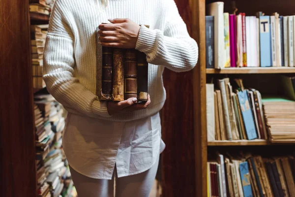 Partial view of woman in white sweater holding books in library — Stock Photo