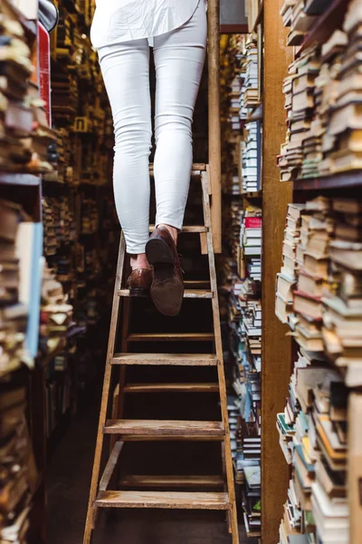 Vue recadrée de la femme debout sur une échelle en bois dans la bibliothèque — Photo de stock