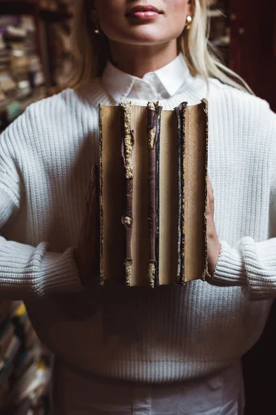 Vue recadrée de la femme en pull blanc tenant des livres rétro dans la bibliothèque — Photo de stock