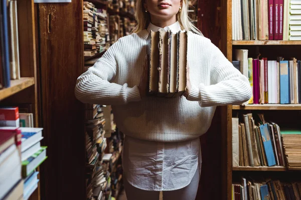 Vista parcial de la mujer en suéter blanco sosteniendo libros retro en la biblioteca - foto de stock