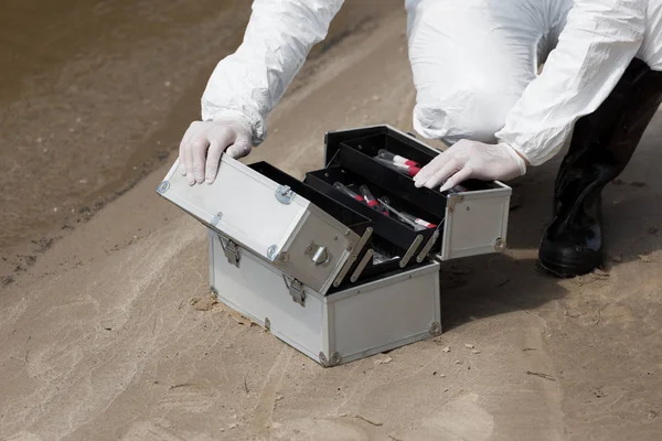 Cropped view of water inspector in latex gloves opening kit with test tubes on sandy coast — Stock Photo