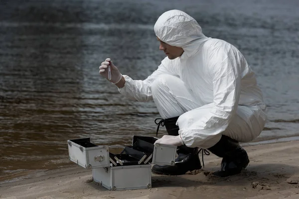 Water inspector in latex gloves and protective costume opening inspection kit on sandy coast — Stock Photo