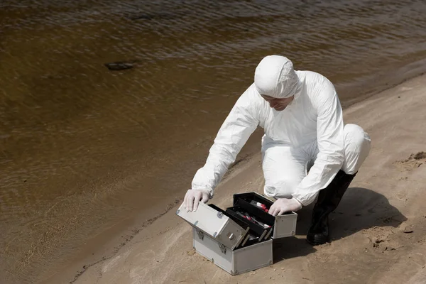 Water inspector in latex gloves and protective costume opening inspection kit on sandy coast — Stock Photo