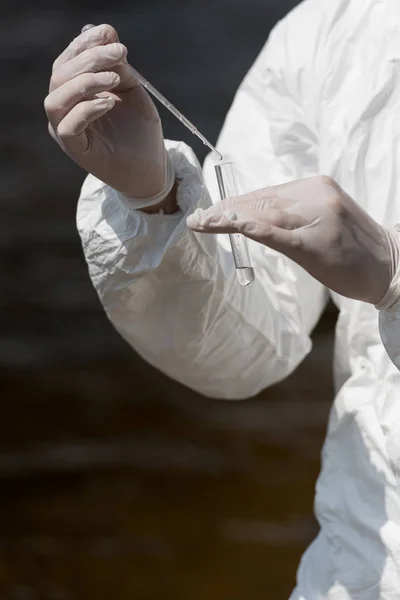 Vista parcial del inspector de agua en guantes de látex con tubo de ensayo tomando muestra de agua - foto de stock