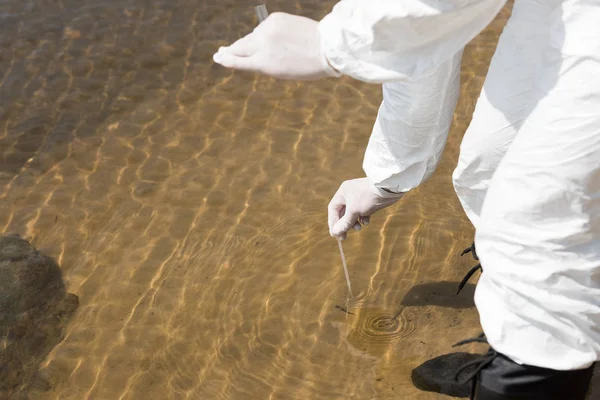 Vue partielle de l'inspecteur de l'eau dans des gants en latex avec éprouvette prélevant un échantillon d'eau — Photo de stock