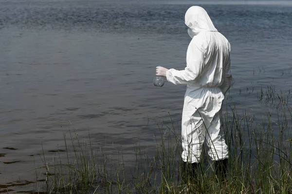 Water inspector in protective costume holding flask while standing near river — Stock Photo