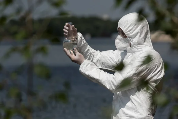 Messa a fuoco selettiva dell'ispettore dell'acqua in costume protettivo, respiratore e occhiali che tengono il pallone con il campione d'acqua — Foto stock